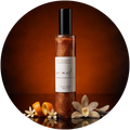 A bottle of Mawamo Oracle body oil with shimmering amber liquid, set against a dark brown circular background with orange slices and white flowers at the base.