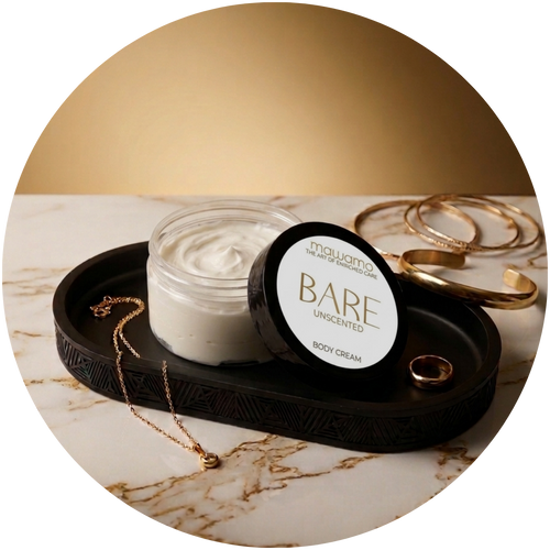 A jar of mawamo body cream with its lid off, placed on a black tray with gold jewelry on a marble surface, with a soft gold background.